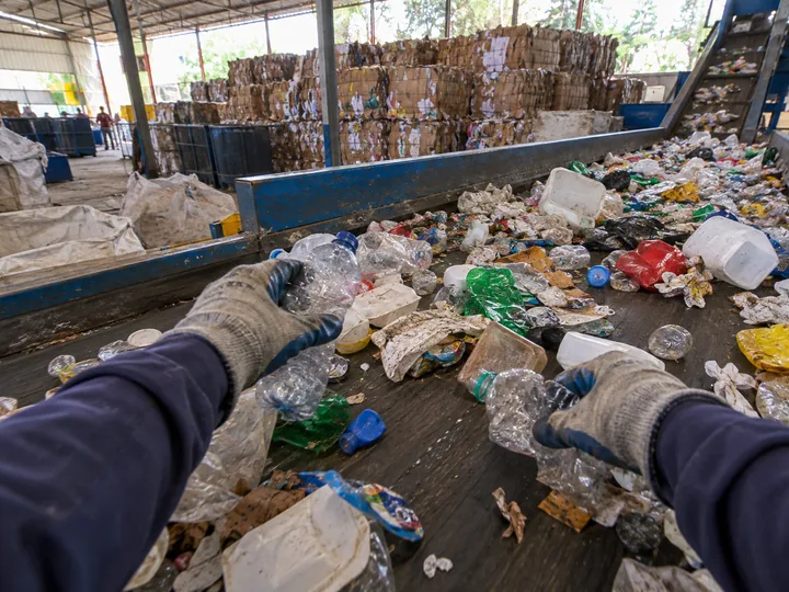 Gloved hands picking plastic bottles off a recycling conveyor belt