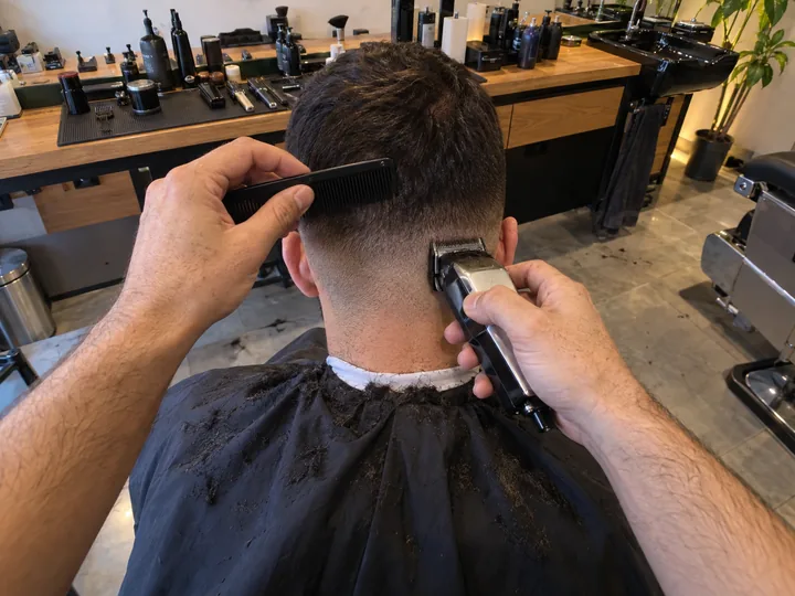Hands with a comb and clippers fading the back of a client's hair
